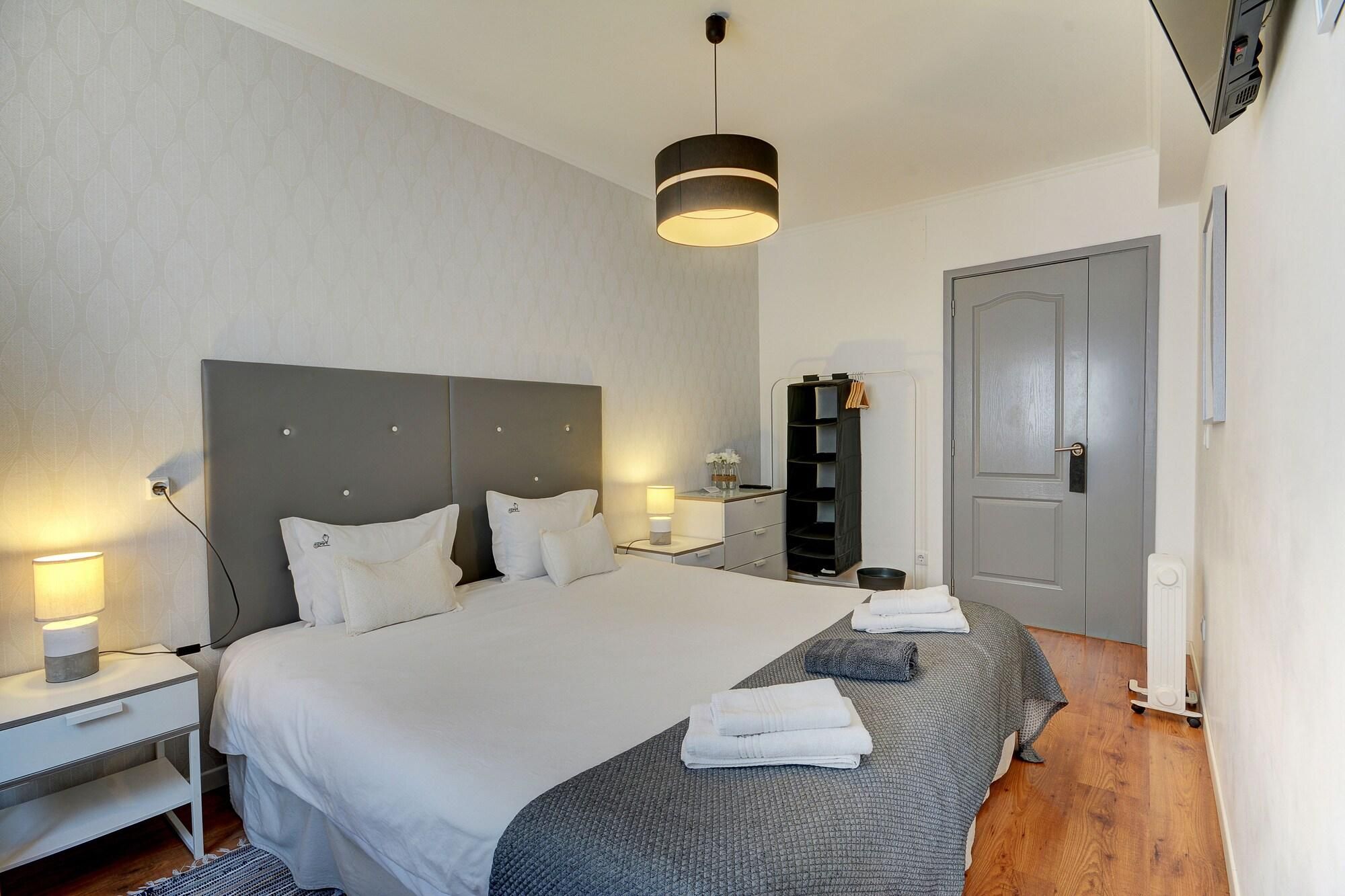 A modern hotel room with a large bed, bedside tables, a wardrobe, and a door.