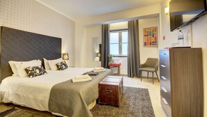 A hotel room with a large bed, a wooden chest, a desk with a chair, and a wardrobe.