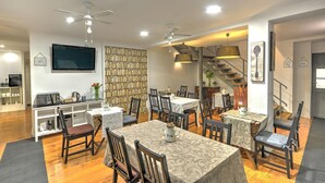 A dining area with multiple tables and chairs, a bookshelf, a television, and a staircase leading to an upper level. - Hostel Innba Lisbon (Braga)