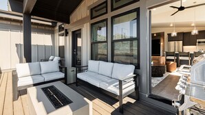 Un espacio exterior moderno con terraza de madera, dos sofás blancos, una mesa de centro y un ventilador de techo.