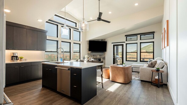 Una cocina moderna con una isla central, muebles oscuros y una zona de comedor con sofá y mesa de centro.