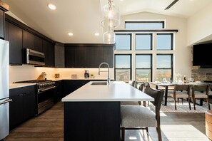 Une cuisine moderne avec des meubles de couleur sombre, des appareils en acier inoxydable et un grand îlot central doté de tabourets de bar.