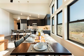 Une cuisine moderne avec des meubles de couleur sombre, des appareils en acier inoxydable et un coin repas doté d’une table en bois, mise pour six personnes.