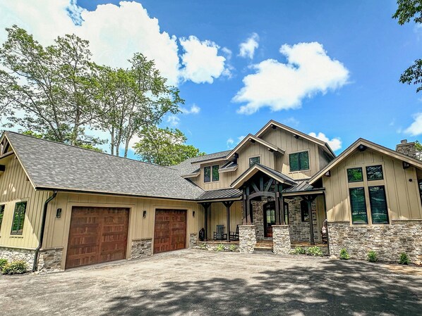 A large, two-story house with a stone foundation, multiple garage doors, and a covered front porch.