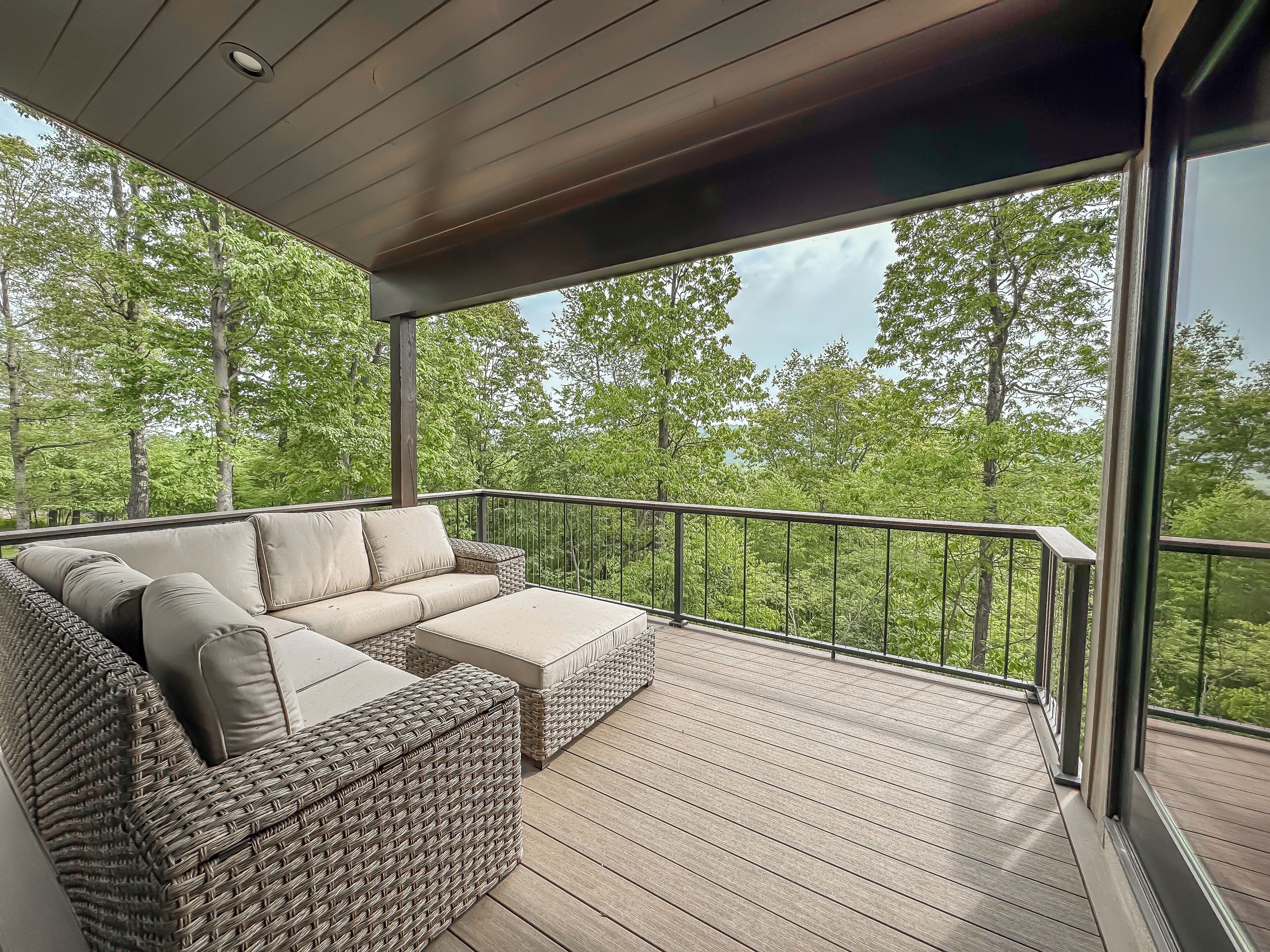 A covered outdoor deck with wicker furniture and a view of a forest.