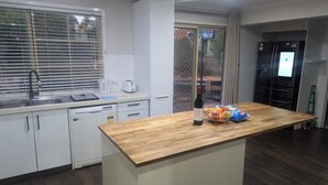 Una cocina moderna con armarios blancos, encimera de madera, un lavabo, un tostador, un hervidor, una botella de vino y una cesta de fruta.