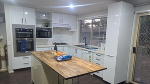 Una cocina moderna con armarios blancos, encimera de madera y horno empotrado.