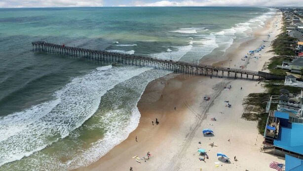 A beach with a pier extending into the ocean, a sandy shore, and beach umbrellas. - The Iron Seahorse by Carolina Getaway - Rooftop Deck & Stunning Ocean Views (Surf City)