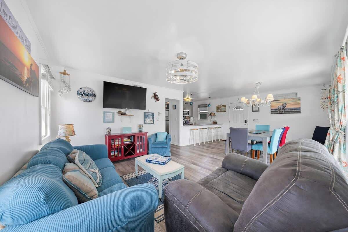 A modern living room with a sofa, a coffee table, and a TV. There is a kitchen area with a dining table and chairs.
