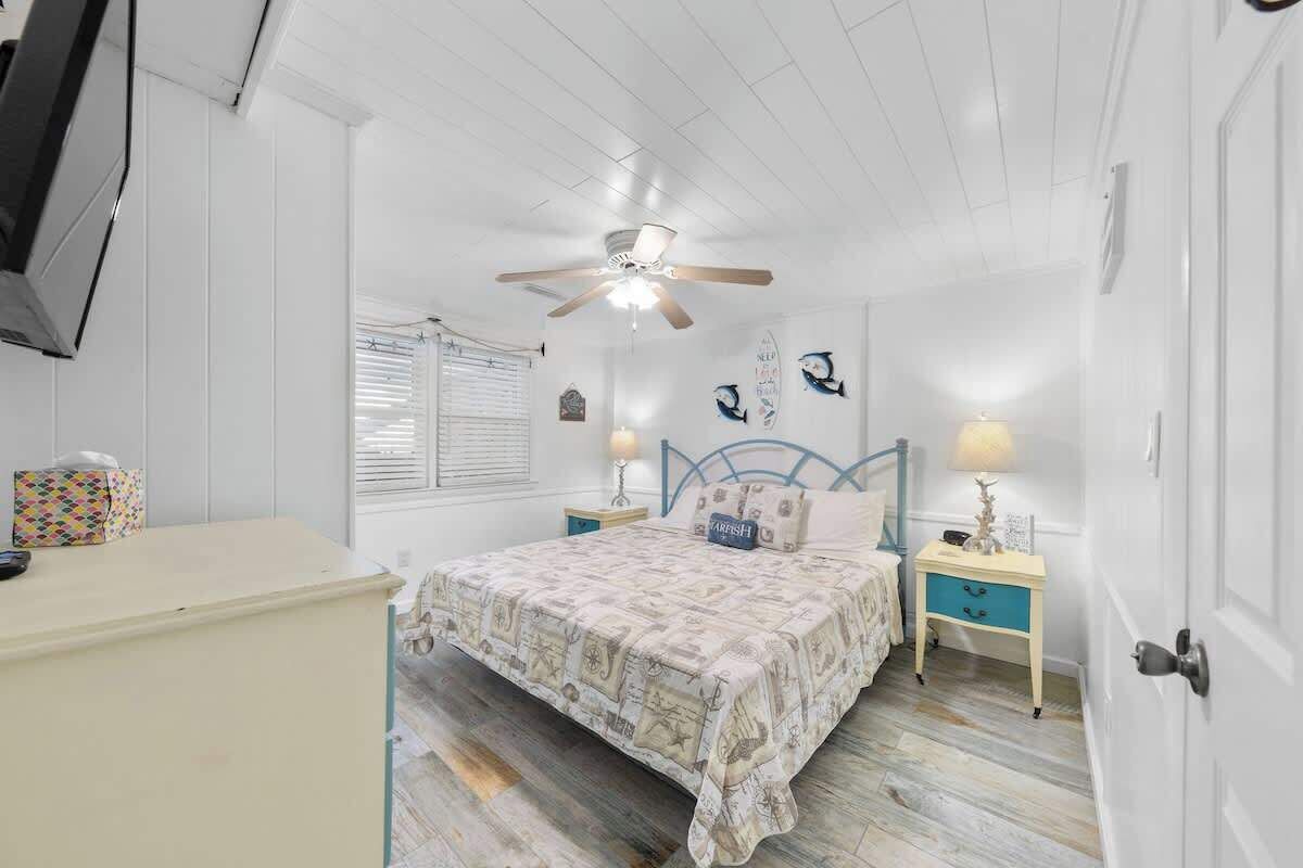 A bedroom with a bed, nightstands, a ceiling fan, a dresser, and a window with blinds.
