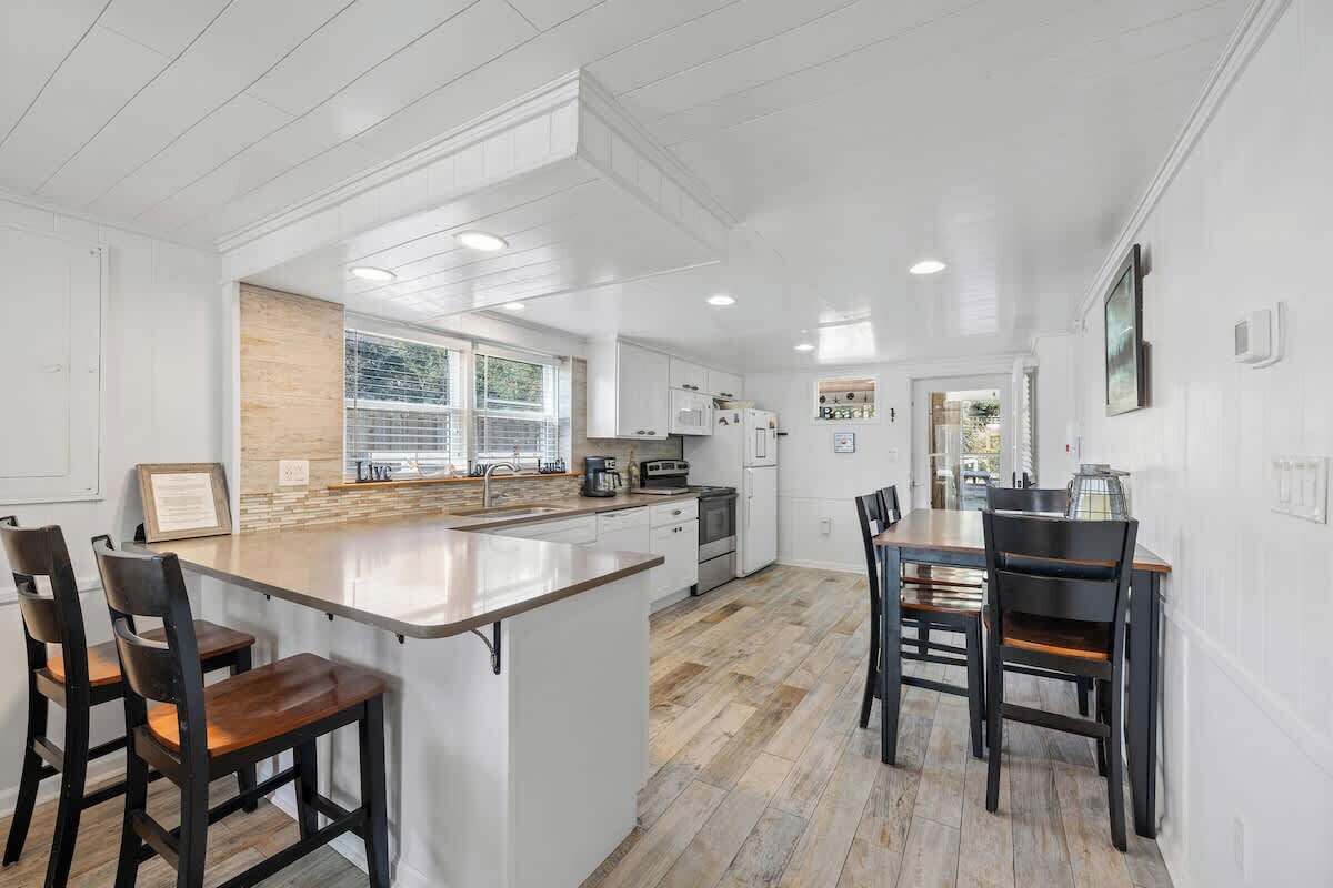 A modern kitchen with white cabinetry, a wooden island, and a dining area with dark chairs.