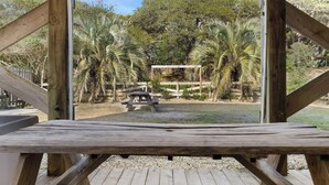 A wooden deck with a view of a fenced outdoor area with palm trees and a picnic table. - The Iron Seahorse by Carolina Getaway - Rooftop Deck & Stunning Ocean Views (Surf City)