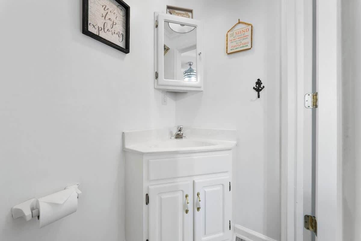 A bathroom with a white vanity, a mirror, a framed quote on the wall, and a hanging sign.
