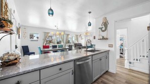 A modern kitchen with a large island, pendant lights, and a view to the dining area. - The Iron Seahorse by Carolina Getaway - Rooftop Deck & Stunning Ocean Views (Surf City)