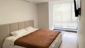 A bedroom with a bed, a window, and a wall-mounted TV. - Departamento de lujo-Torre Gante 302 (Quito)