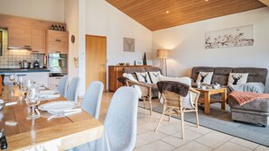 A spacious living area with a dining table set for six, a sofa with deer-themed cushions, and a kitchen in the background. - Le Souvenir by Interhome (Ovronnaz)
