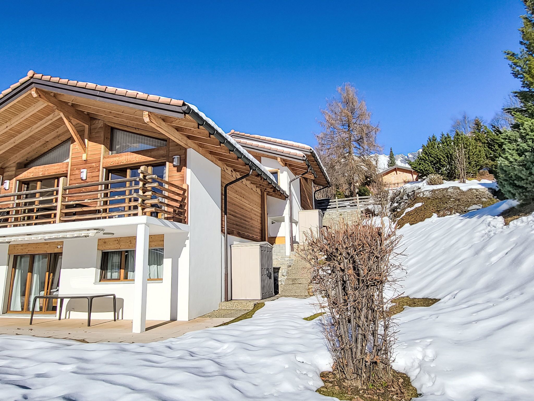 A wooden chalet with a balcony, a covered patio, and a snow-covered landscape.