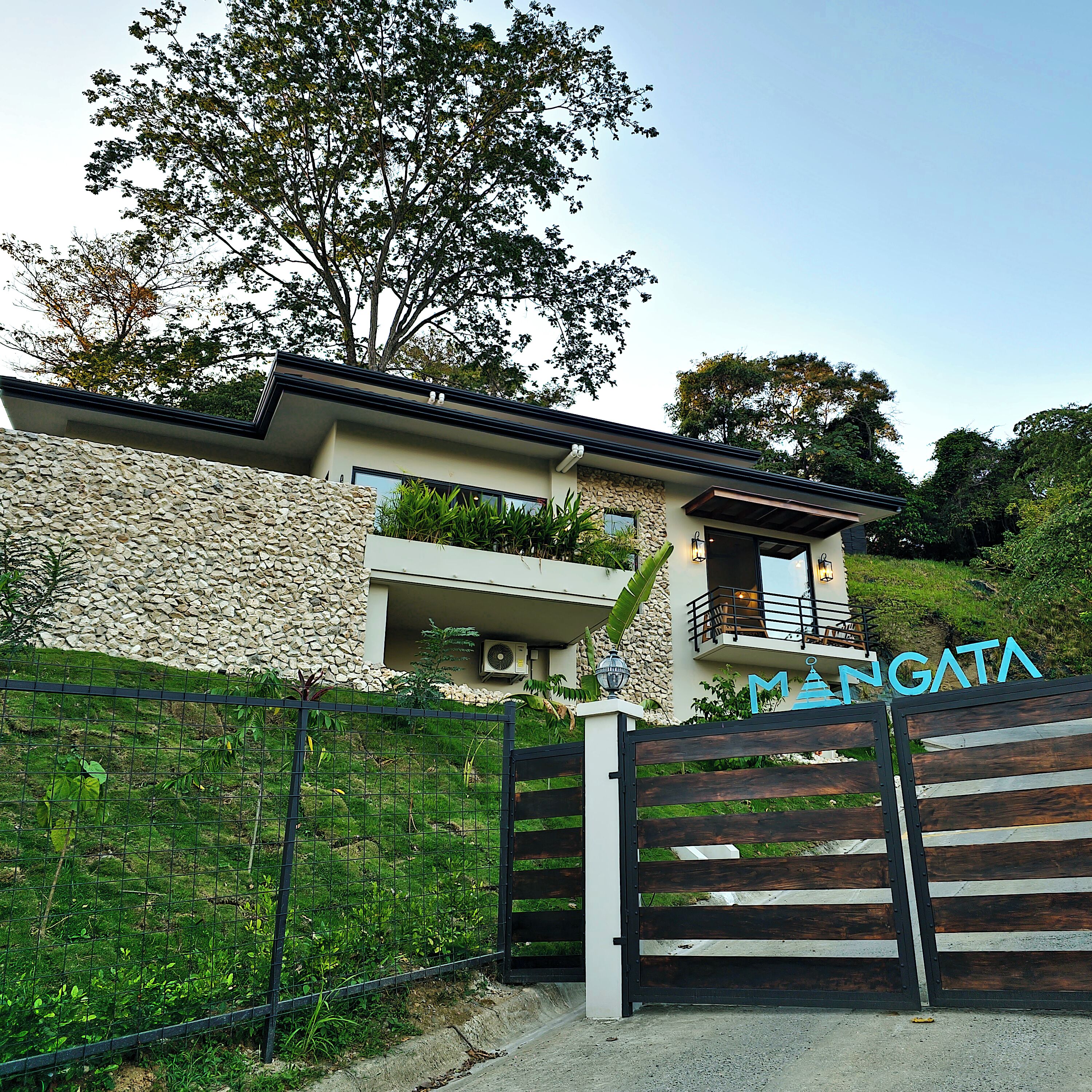 A modern house with a stone facade, a balcony, and a gated entrance.