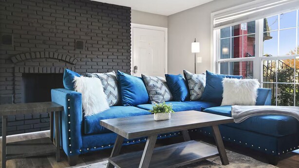 A living room with a blue sofa, a fireplace, and a large window. - Centrally Located Apt with Pool in Columbia, MO (Columbia)