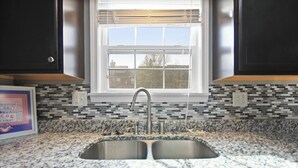A kitchen with a double sink, a window with blinds, and a backsplash with mosaic tiles. - Centrally Located Apt with Pool in Columbia, MO (Columbia)
