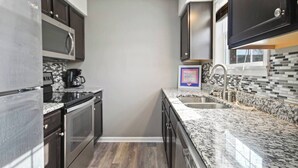A modern kitchen with dark cabinetry, a granite countertop, and a stainless steel sink. - Centrally Located Apt with Pool in Columbia, MO (Columbia)