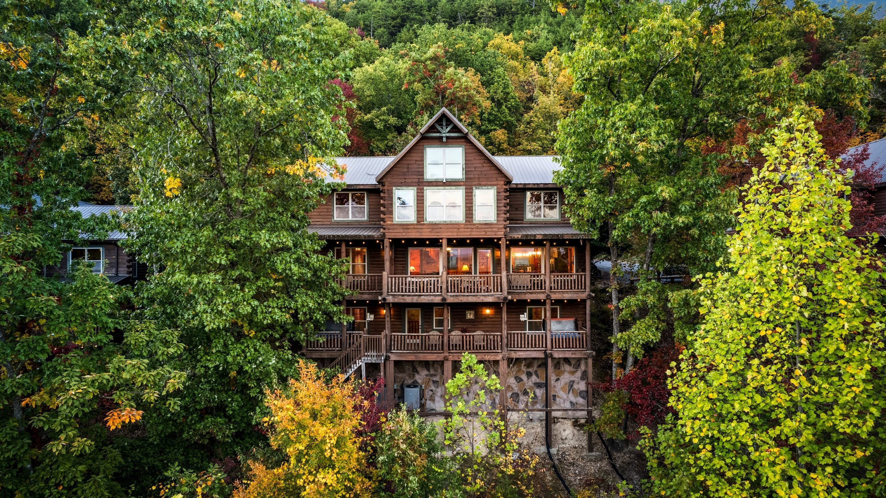 A multi-story log cabin with a stone foundation, surrounded by dense forest.