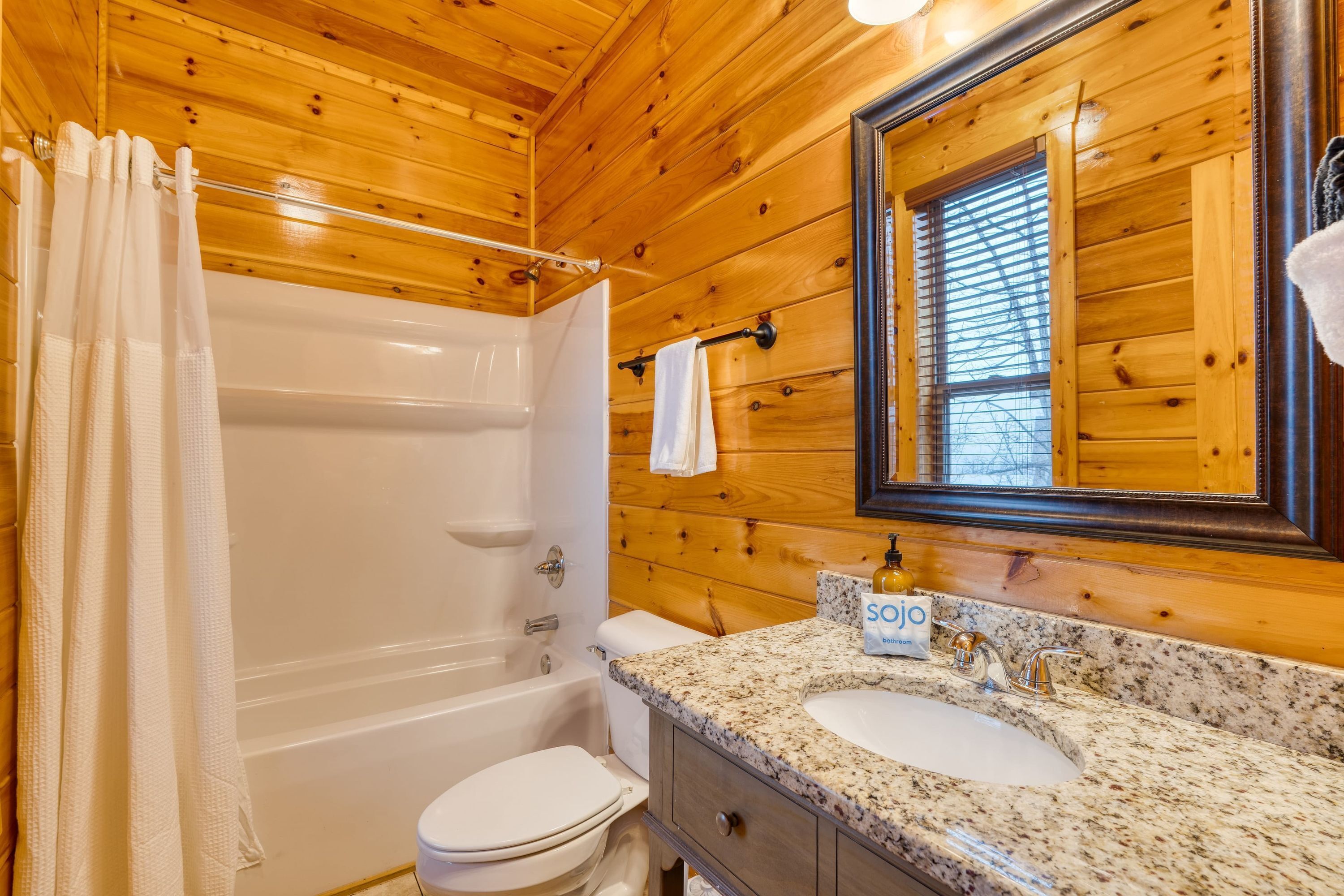 Un baño de cabaña de madera con bañera, inodoro y lavamanos con dispensador de jabón.