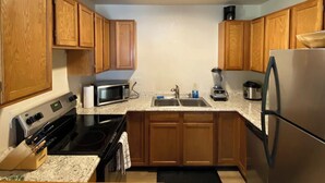 Cocina compacta con armarios de madera, microondas, estufa, pileta y refrigerador.