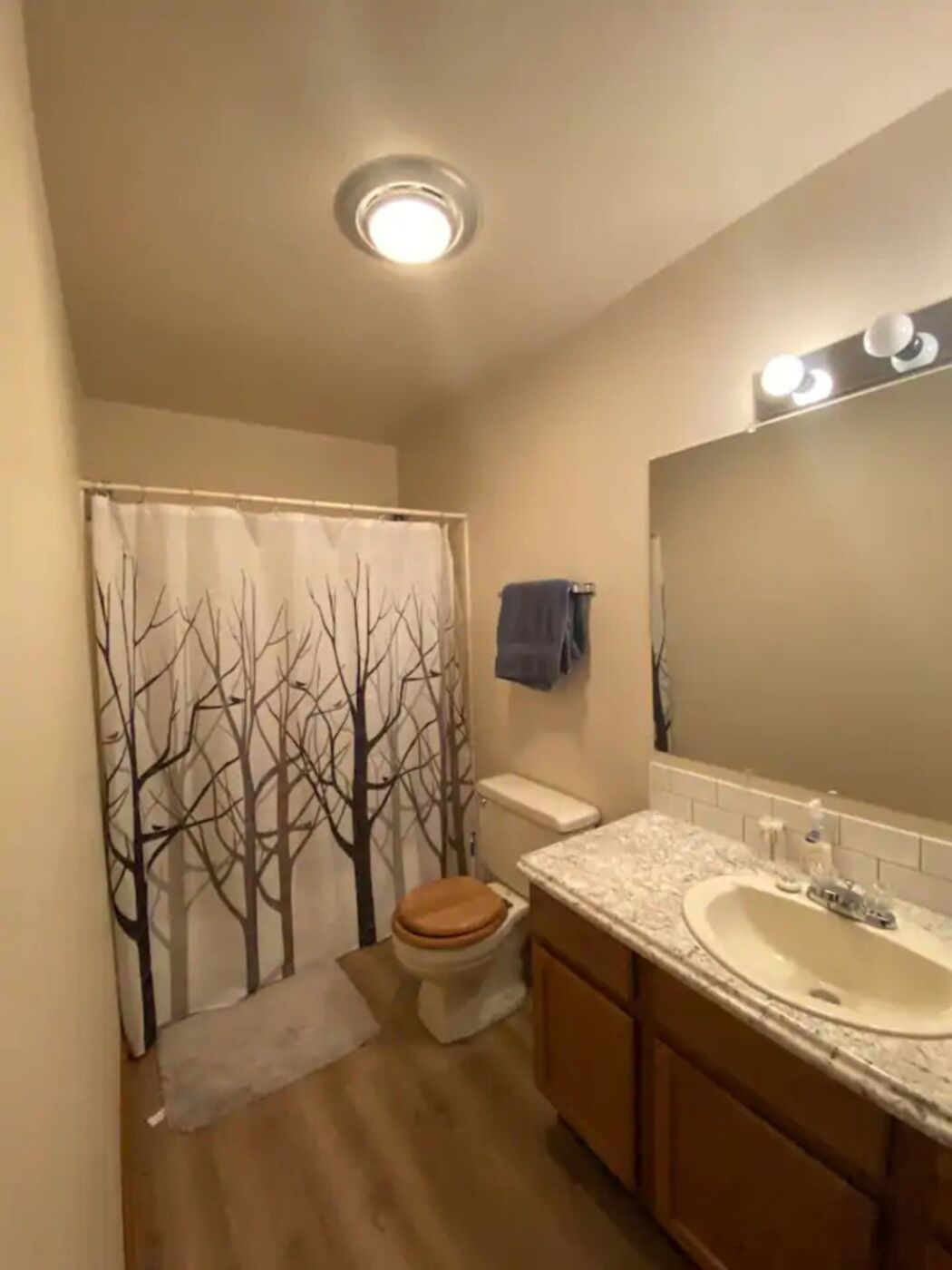 Un bagno con il water, lavandino e tenda da doccia con motivo alberi.