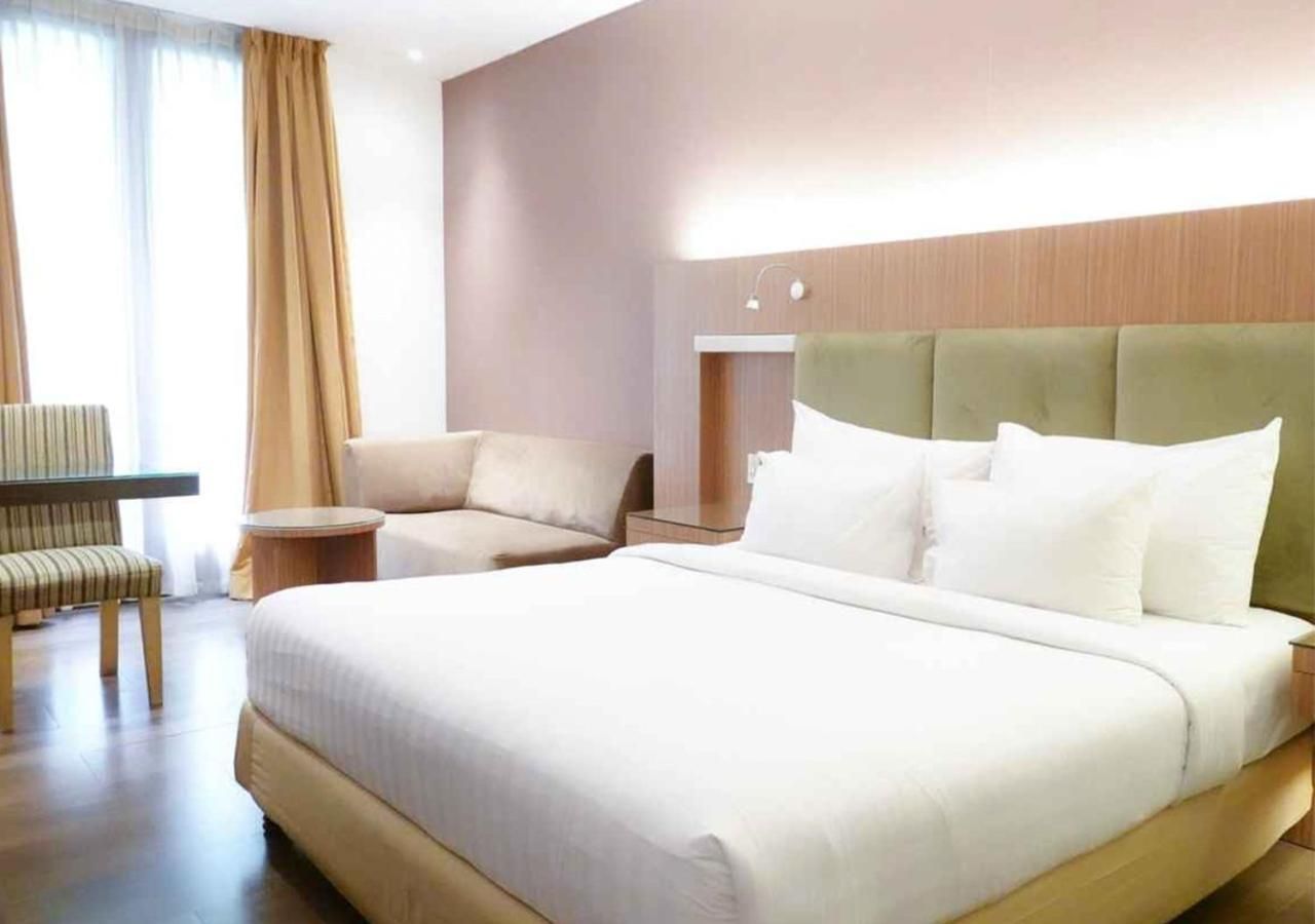 A hotel room with a large bed, a seating area with a chair and a small table, and a window with curtains.