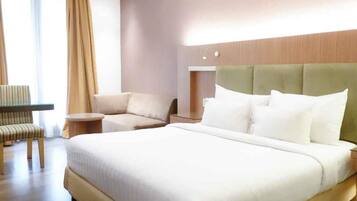 A hotel room with a large bed, a seating area with a chair and a small table, and a window with curtains.