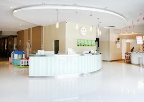 A modern reception area with a curved counter, pendant lighting, and a children's play area. - Hotel Wisata Niaga (Purwokerto)