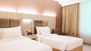 Habitación de hotel con dos camas, una mesita de noche con lámpara, una silla y un ventanal con cortinas.