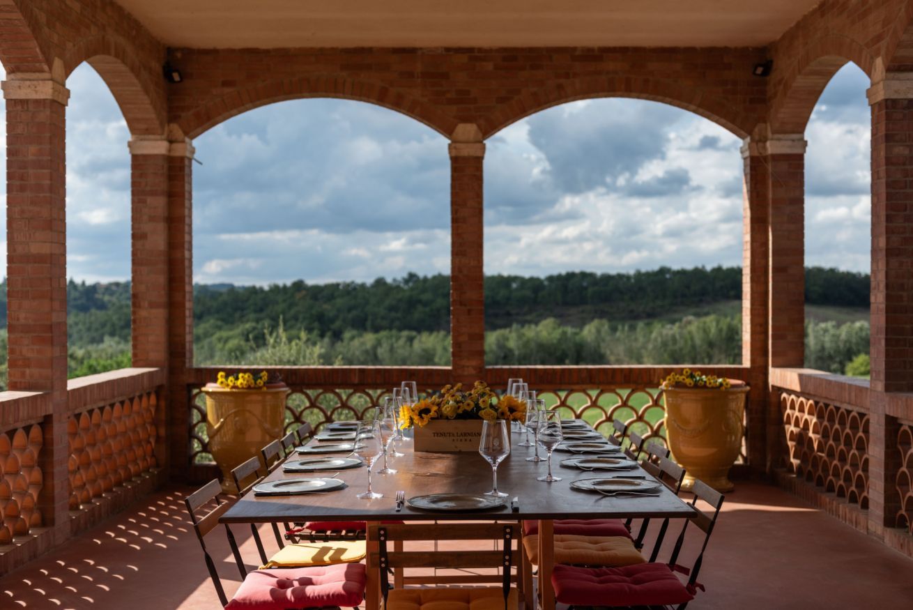 A dining table set for four with a view of a forested landscape through an arched brick structure.