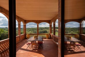 A covered terrace with a table set for dining, overlooking a lush landscape.