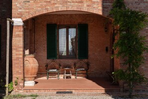 A brick building with a covered patio area featuring two metal chairs and a small table.