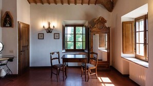 Une pièce avec une table et des chaises en bois, une fenêtre donnant sur un paysage agréable, une horloge murale et un radiateur.