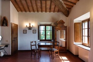 Una stanza con un tavolo e sedie in legno, una finestra con vista, una sveglia appesa al muro e un termosifone.