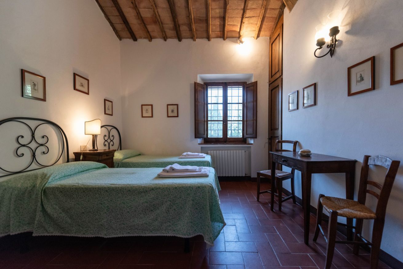 Una habitación con dos camas, una mesa, sillas, un radiador y una ventana con vistas.