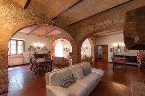 Un espacio habitable amplio con techo alto, arcos de ladrillo visto, un sofá, una mesa de comedor con sillas y una mesa de fútbol de mesa.