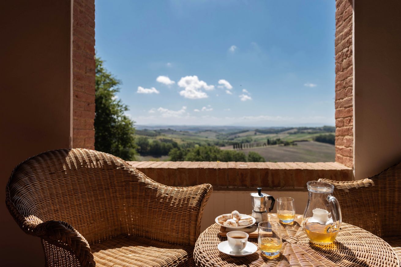 A wicker chair and table with a view of rolling hills and a clear sky.