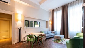 Een moderne woonkamer met een houten vloer, een grijze bank, een groene fauteuil en een eettafel met stoelen.