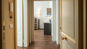 Een gang die leidt naar een keuken met een houten vloer, witte muren en een zichtbare lichtschakelaar.