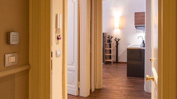Een hal met een houten vloer die leidt naar een keuken met een spoelbak en kastjes.