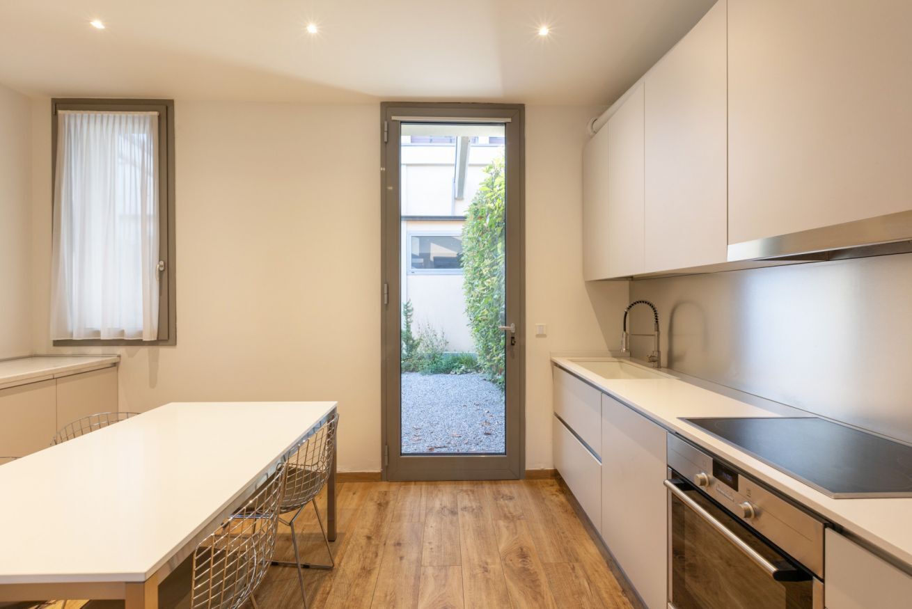 A modern kitchen with a white countertop, stainless steel appliances, and a door leading to a garden.