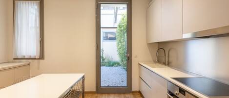 A modern kitchen with a white countertop, stainless steel appliances, and a door leading to a garden.