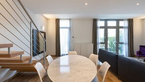 A modern living room with a marble dining table, white chairs, a black sofa, and a staircase. - Beautiful two bedrooms Navigli - Mirable PM (Milano)