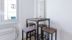 Pieni, moderni huone, jossa on valkoinen patteri, ikkuna ja pöytä sekä siihen sopivat jakkarat.