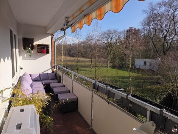 A balcony with a seating area, a view of a grassy field, and a white trailer in the background.