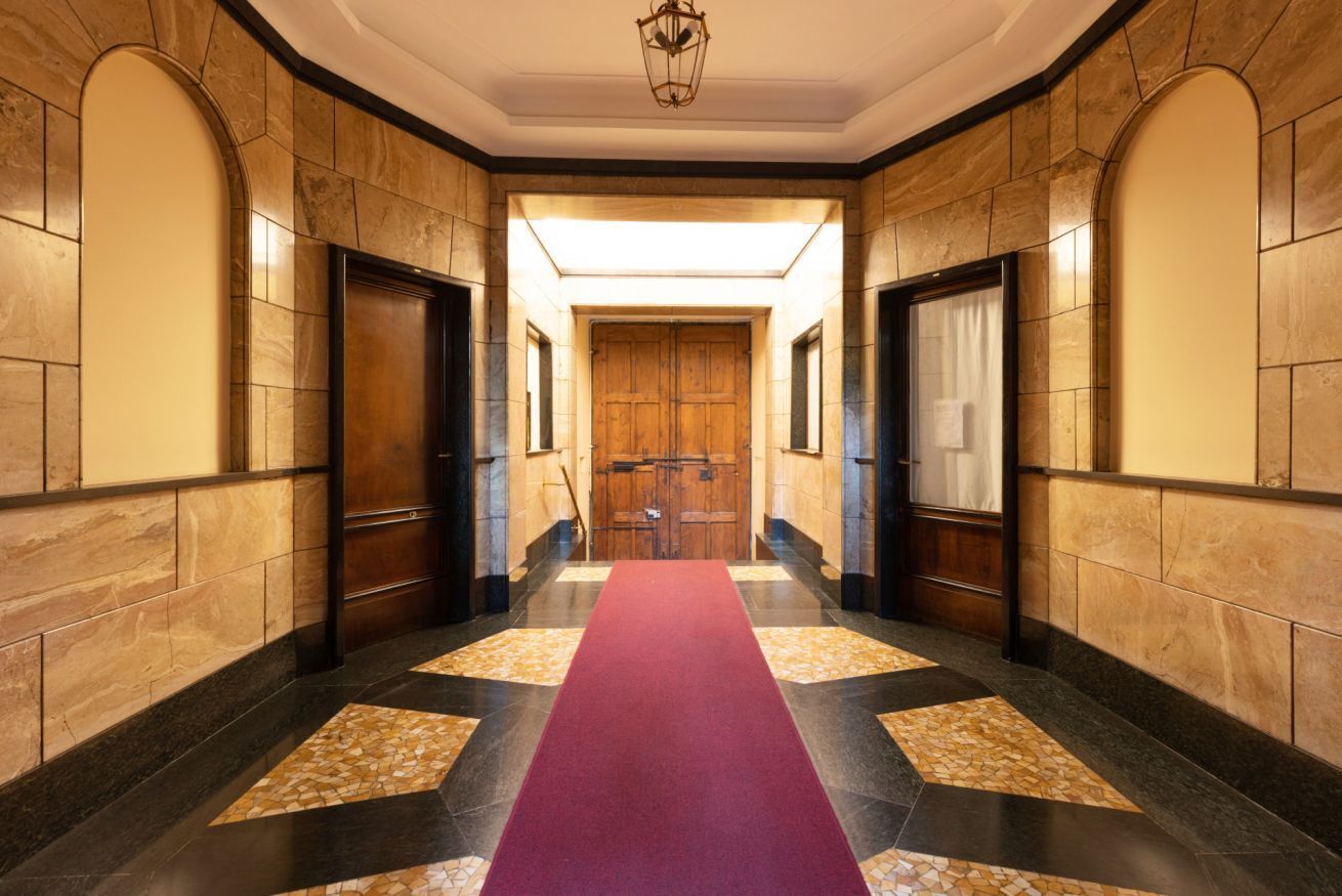 A hallway with a red carpet, wooden doors, and a large wooden door at the end.